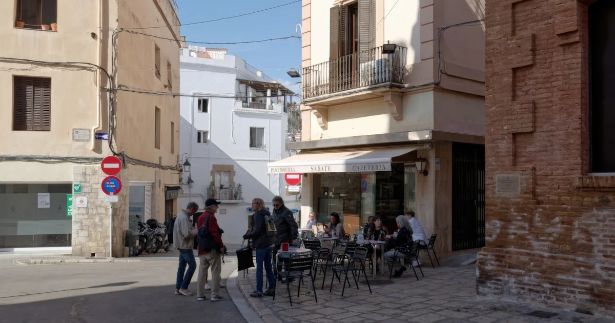 Personas sentadas en terrazas de café en una calle soleada