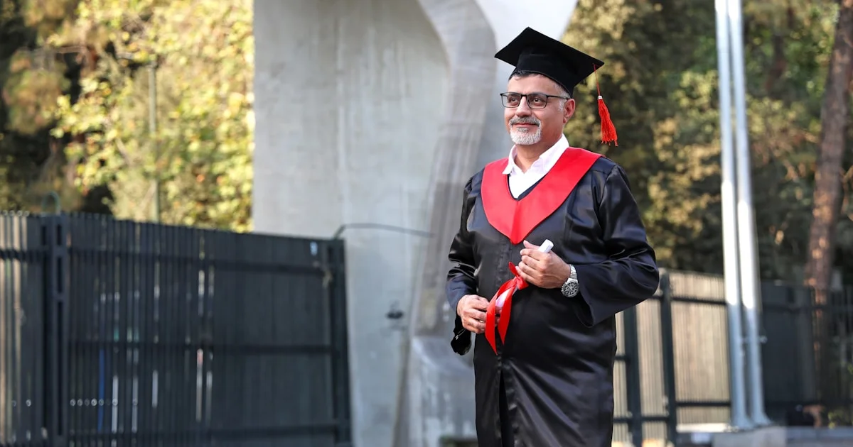 Hombre con toga de graduación sujetando diploma al aire libre