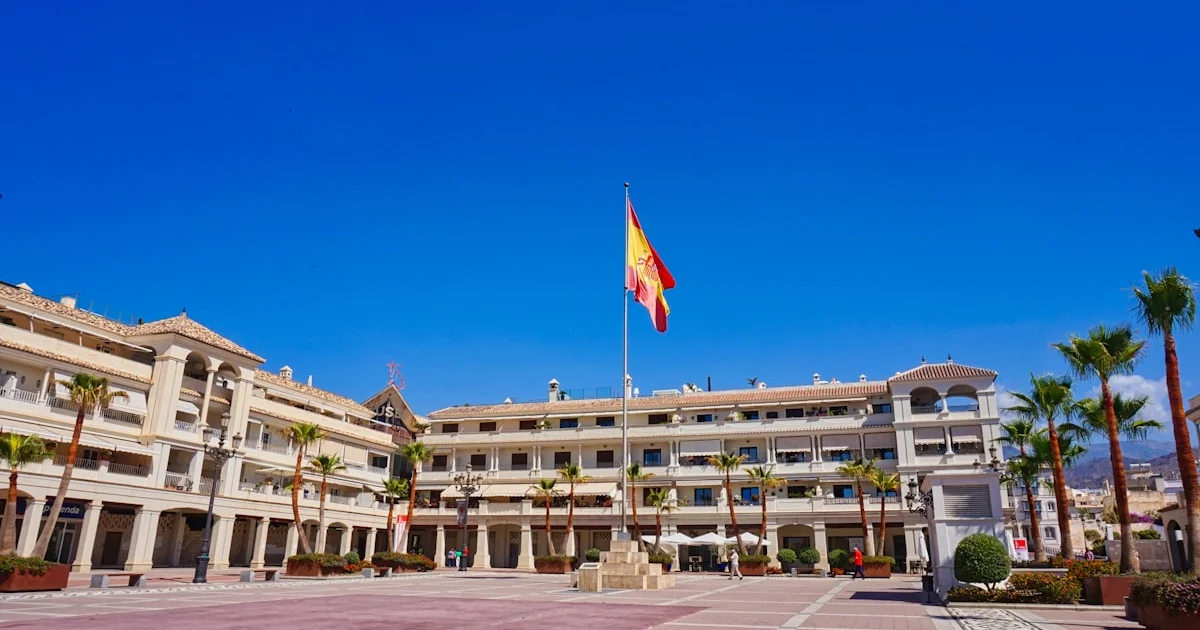 Square with official building, Spanish flag and palm trees in Nerja